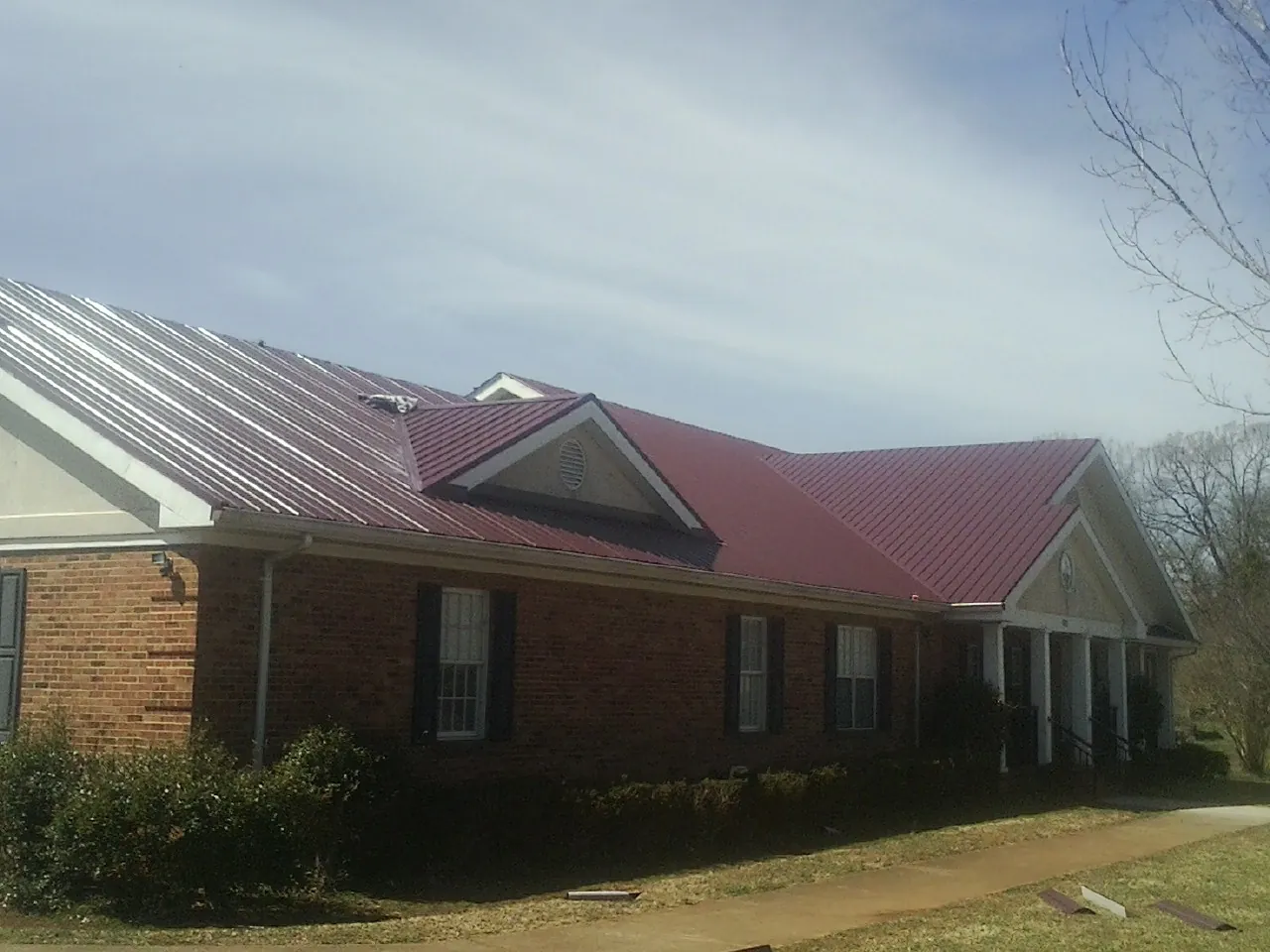 Red metal roof with gabled entries on a long brick building, from a Hail Damage Roof Repair job in Lincoln